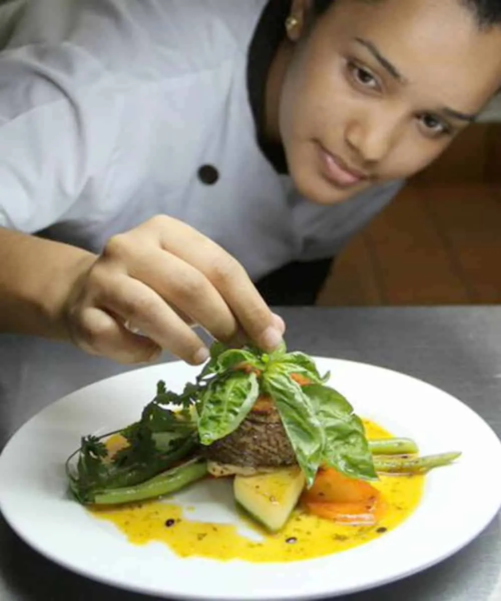 A female chef preparing a plate of food.