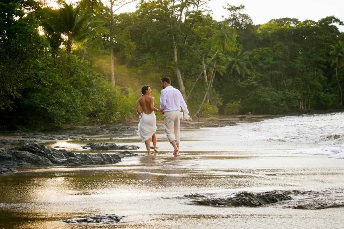 A bride and groom walking on a beach in costa rica.